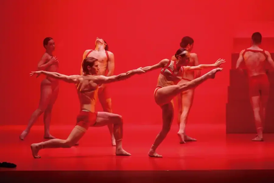 Seis bailarines con trajes rojos y beige actúan en el escenario bajo una iluminación roja. Con coreografía de Víctor Jiménez, los bailarines evocan el drama de Don Juan cuando dos de ellos, en primer plano, se cogen de la mano mientras otros posan detrás bailando expresivamente.
