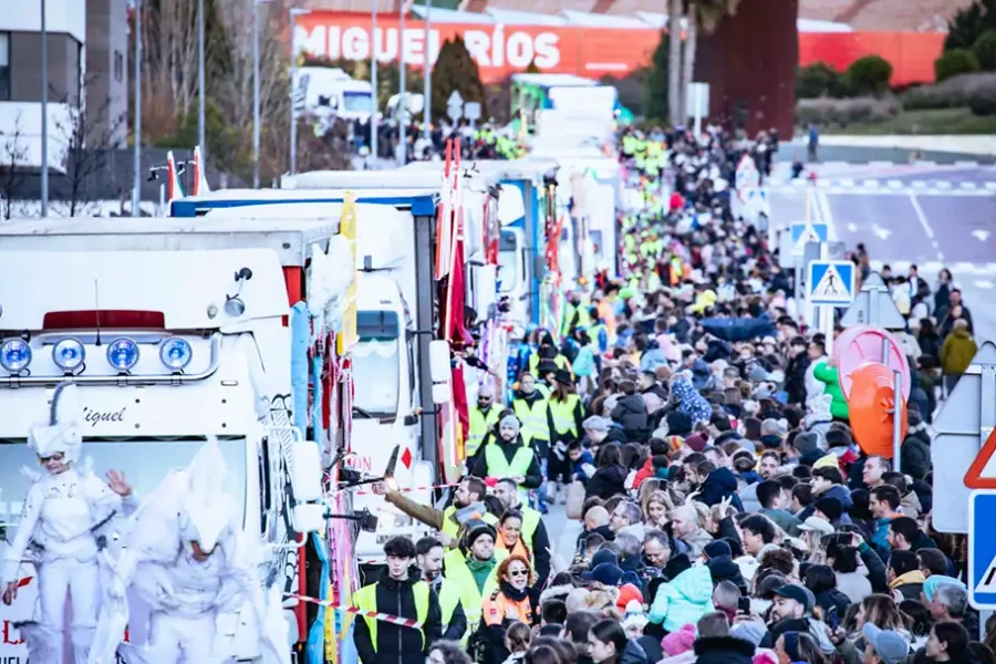 Una gran multitud se agolpa en una calle de Rivas llena de carrozas decoradas y gente disfrazada durante el desfile de la Cabalgata de Reyes. Muchos asistentes llevan abrigos y personal de seguridad con chalecos amarillos recorre el trayecto.