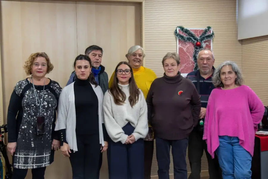Ocho adultos están de pie en el interior, en fila india, mirando a la cámara. El ambiente parece informal, con una corona navideña en la pared detrás de ellos. Todos están vestidos con ropa de diario, lo que sugiere una reunión amistosa de Cohabita Rivas.