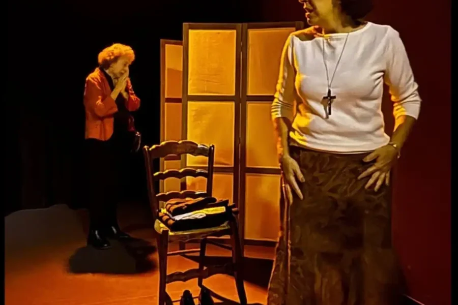 Dos mujeres de pie en un escenario poco iluminado con una silla y un abrigo al fondo. Texto muestra MORTAJA, una obra de teatro sobre crímenes del franquismo, créditos, nombres del reparto y detalles del evento para el sábado 31 de enero a las 20:00.