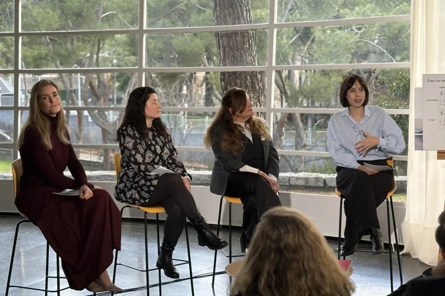 Cuatro mujeres sentadas en taburetes frente a grandes ventanales durante una mesa redonda sobre ciencia climática. Una mujer a la derecha habla, mientras las otras escuchan atentamente. El público está sentado en primer plano.