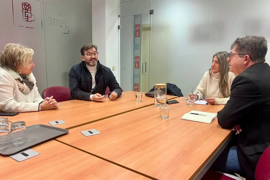 Cuatro personas se sientan alrededor de una mesa de conferencias en la sala de reuniones de una oficina, discutiendo ideas para apoyar el tejido empresarial local. Sobre la mesa hay vasos de agua, cuadernos y bolígrafos. Al fondo, paredes de cristal y una puerta.