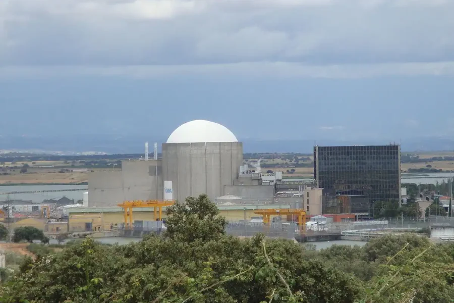 Una central nuclear con un gran edificio de contención en forma de cúpula blanca se alza entre arbustos y campos bajo un cielo nublado, mientras los ecologistas en acción expresan su preocupación por su impacto en el paisaje rural.