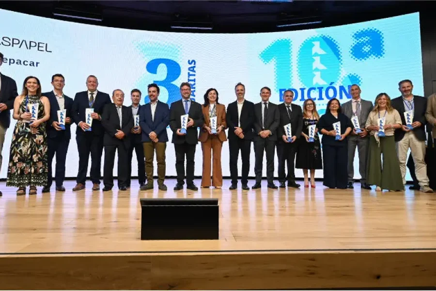 Un grupo de dieciocho personas vestidas con traje de negocios posa en un escenario con los premios en la mano, para una foto frente a una gran pantalla en la que se muestran datos del evento y los logotipos de los patrocinadores.