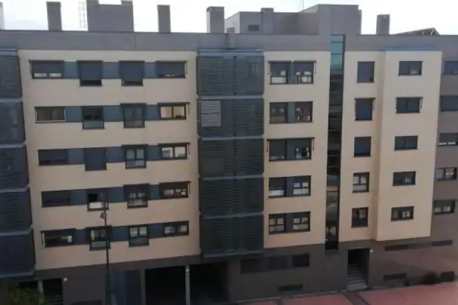 Un moderno edificio de apartamentos de varias plantas con paredes exteriores de color beige y gris, numerosas ventanas y algunos balcones refleja el cambiante horizonte de España a medida que crece la preocupación por los hogares hacinados en toda la UE. Al fondo se ve vegetación.