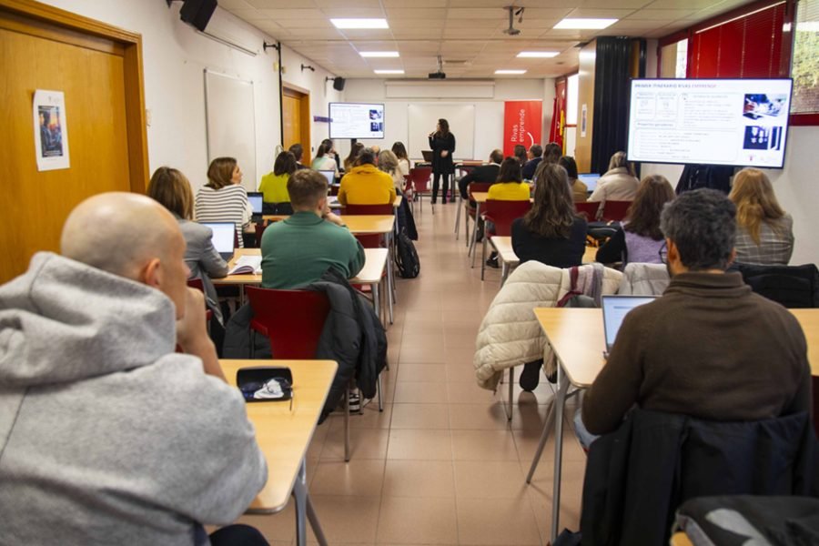 Aula con una veintena de personas asistentes a una formación y una docente exponiendo ante las pantallas de proyección, en Rivas Vaciamadrid