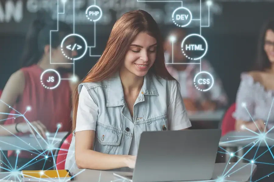 Una joven sentada en un escritorio utilizando un ordenador portátil. Sobre la imagen se superponen gráficos digitales que destacan conocimientos de programación como HTML, CSS, JS, PHP, DEV y Verifactu. La escena sugiere oportunidades de formación para empresas locales. Otras personas aparecen difuminadas en el fondo.