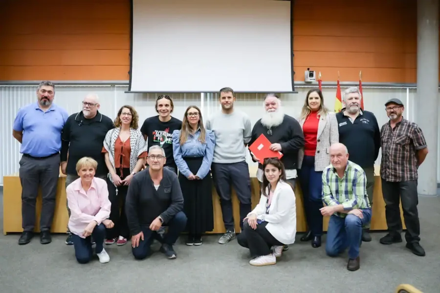 Un grupo de quince adultos posa en el interior frente a una pantalla de proyector en blanco, probablemente durante un acto de cooperación internacional o una reunión de convenios en Rivas. Algunos están de pie, otros arrodillados o sentados, vestidos de manera informal en un aula o sala de conferencias.