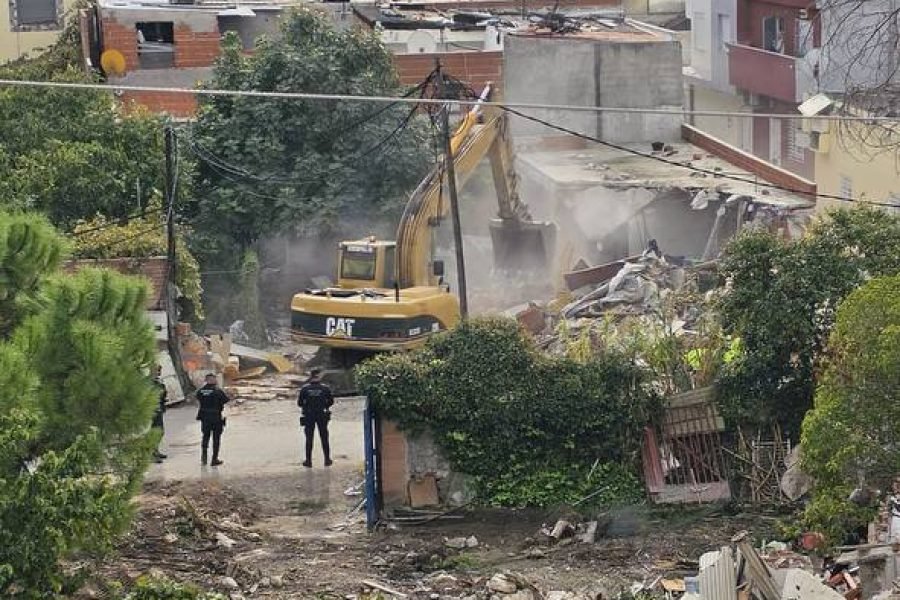 Excavadora derribando una infravivienda en la Cañada Real, con escombros en primer plano y agentes de seguridad