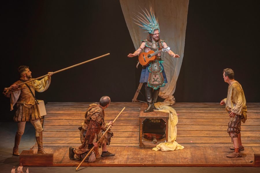 Cuatro actores sobre el escenario en una escena de «La desconquista»: uno con un tocado de plumas y guitarra, otros dos con lanzas y otro con ropas raídas