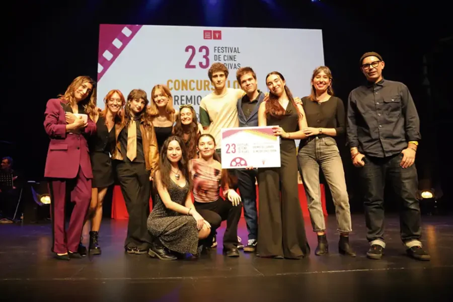 Un grupo de doce personas posa en el escenario, algunas de pie y otras arrodilladas, sosteniendo un gran certificado. Detrás de ellos, una pantalla muestra 23 Festival de Cine Rivas con texto adicional. El escenario parece ser un acto de entrega de premios de edición de vídeo o montaje.