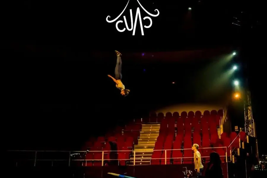Gran Gala Circo. Una oscura pista de circo con un artista en el aire sobre un trampolín, asientos rojos vacíos y focos. El texto en blanco dice "Gran Gala Circo, 13 Septiembre 2025, 20:00, Auditorio Pilar Bardem". La información sobre las entradas aparece en la parte inferior.