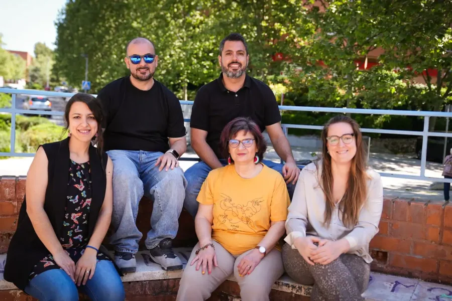 Cinco adultos se sientan en unas escaleras de ladrillo al aire libre en Covibar, posando para una foto de grupo. Los árboles y la vegetación llenan el fondo, con un niño pequeño en la distancia, capturando un momento comunitario que refleja las mejoras en el barrio.