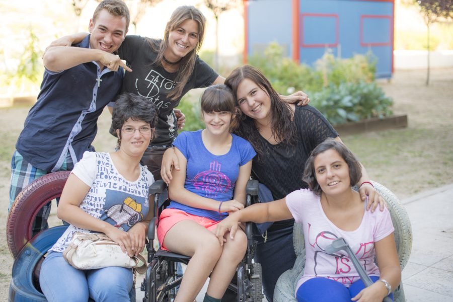 Seis jóvenes integrantes de la asociación El gato de 5 patas, dos de ellos sentados —uno en silla de ruedas—, posan sonrientes en un parque de Rivas