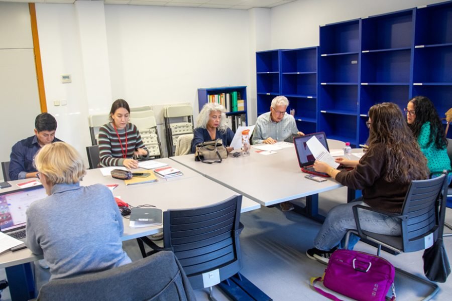 Siete personas del servicio de gestión y resolución de conflictos vecinales trabajan con portátiles y documentos alrededor de dos mesas unidas en una sala luminosa