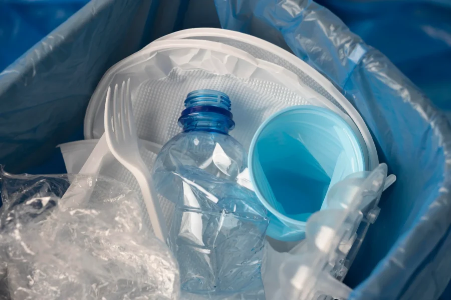 Un primer plano de objetos de plástico desechados, como una botella de agua aplastada, un vaso azul, un tenedor y envases de comida dentro de una bolsa de basura azul, que arrojan luz sobre el creciente impacto en la salud mundial de aquí a 2040.