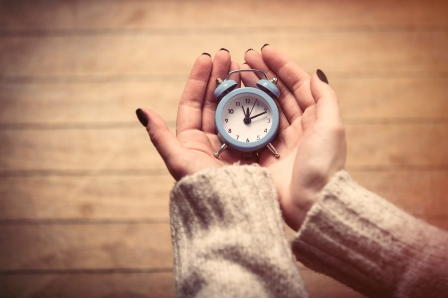 beautiful woman hands holding small blue alarm clock on the wonderful brown wooden background