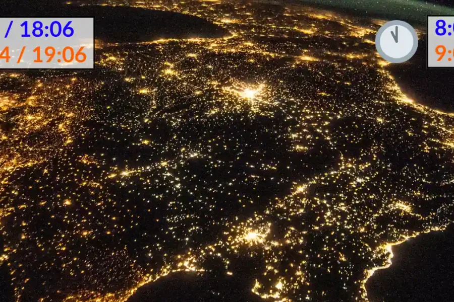 Una vista nocturna por satélite de España y Portugal muestra las luces de las ciudades. Se superponen dos relojes con horas digitales, que reflejan el horario de invierno y el horario de verano, y muestran las 9:04/18:06, 10:04/19:06 a la izquierda, y las 8:00/17:21, 9:00/18:21 a la derecha.