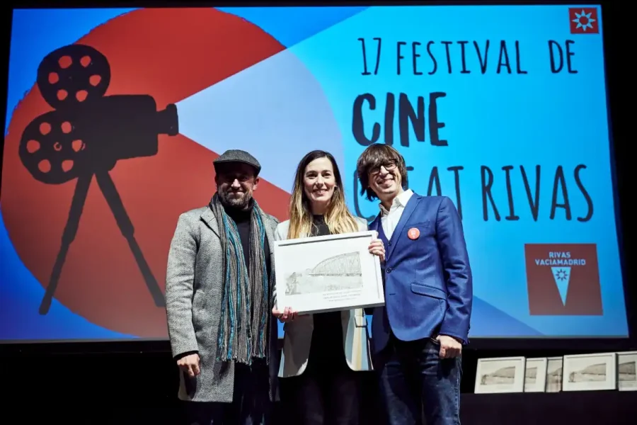 Tres personas sostienen un premio enmarcado en el escenario del Festival de Cine Rivas. Detrás de ellos, una pantalla muestra "17 Festival de Cine Rivas" con el gráfico de un proyector de cine y el logotipo de Rivas Vaciamadrid. Inscripciones 2026 próximamente.