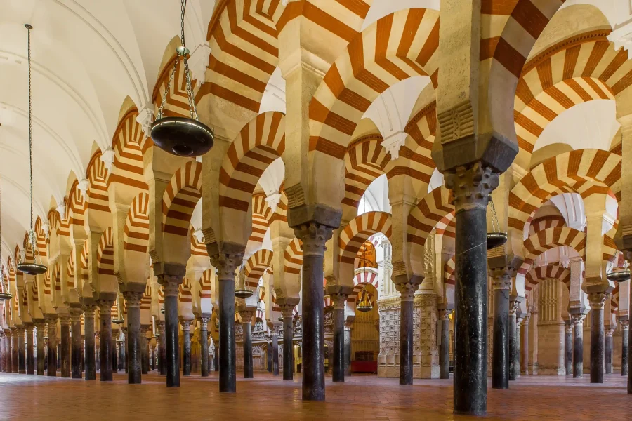 Vista interior de la Mezquita-Catedral de Córdoba que muestra hileras de columnas de piedra y arcos dobles con dovelas rojas y blancas alternadas bajo altos techos abovedados, un ejemplo de renombre entre los bienes inmatriculados.