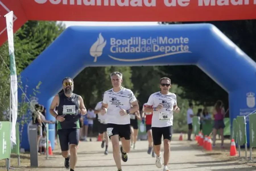Tres hombres corren hacia la línea de meta en una carrera al aire libre que se celebra en Arco Verde, pasando por debajo de un arco hinchable azul y una pancarta roja. Este recorrido panorámico tiene una longitud de 222 kilómetros y conecta 25 municipios de la Comunidad de Madrid.