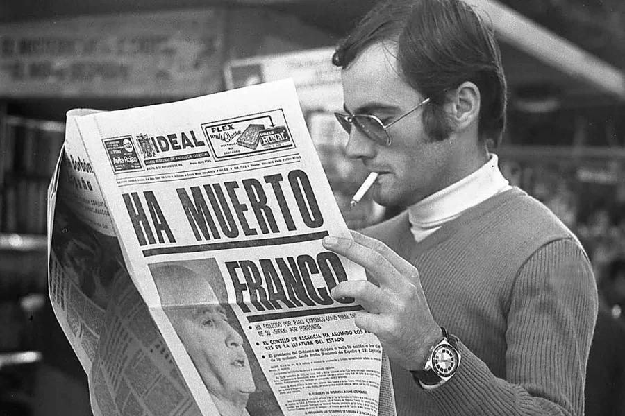 Un hombre con gafas de sol y jersey fuma un cigarrillo mientras lee un periódico con el titular "HA MUERTO FRANCO" y una foto en blanco y negro de Franco en portada, reflexionando sobre las polémicas inmatriculaciones.