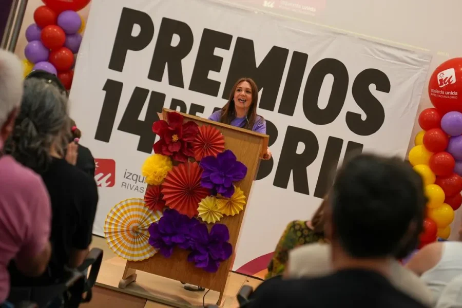 Una mujer sube a un podio decorado en Rivas, dirigiéndose a 500 personas durante las Jornadas Republicanas, con globos de colores y adornos de papel enmarcando una gran pancarta de PREMIOS 14 DE ABRIL detrás de ella.