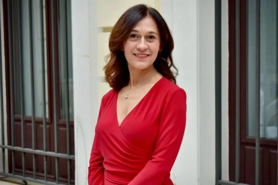 Pilar Trinidad, con el pelo castaño hasta los hombros, lleva un vestido rojo con cuello en V y un delicado collar de plata.