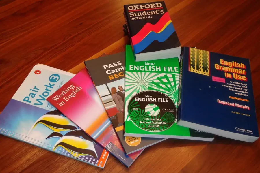 Seis libros de aprendizaje de inglés, ideales para quienes se preparan para la convocatoria o buscan un certificado oficial de inglés C1 de Escuelas de Idiomas, están dispuestos sobre una superficie de madera. Incluye guías gramaticales, un diccionario y material para practicar el examen.