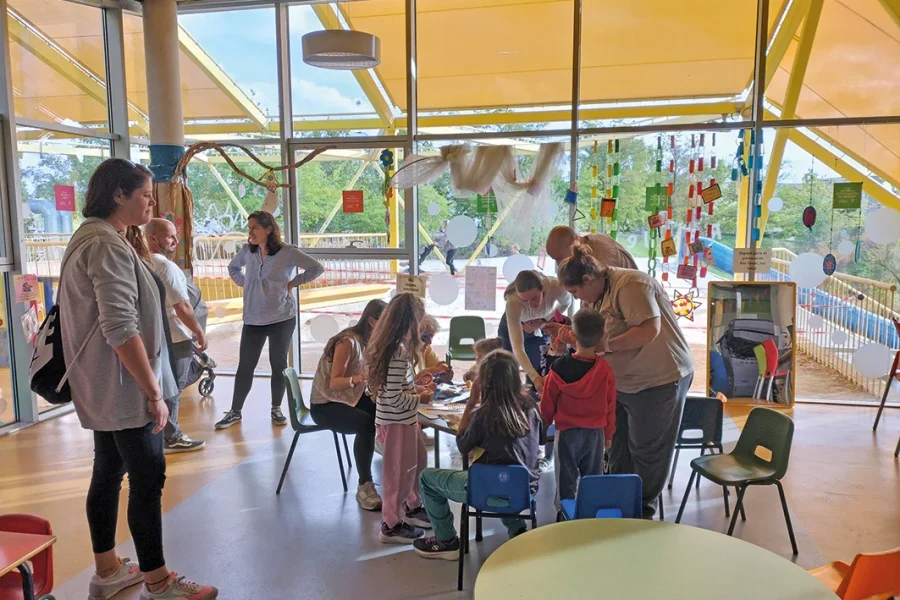 Adultos y niños se reúnen alrededor de una mesa para realizar una actividad artística en un centro comunitario bañado por la luz del sol, participando en las actividades infantiles gratuitas que se organizan en Rivas.